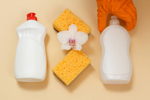 Bouteilles en plastique de liquide vaisselle, détergent pour fours à micro-ondes et poêles avec une main dans un gant en caoutchouc, éponges et une fleur d'orchidée blanche. Vue de dessus. Set de lavage et de nettoyage
. - Photo, image