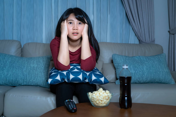Jeune femme asiatique regarder la télévision suspense film ou nouvelles regarder choqué et excité manger pop-corn tard dans la nuit à la maison salon canapé pendant le temps de l'isolement à la maison
 - Photo, image