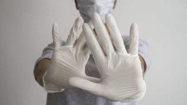 Femme avec un masque médical blanc et un gant en latex montre le symbole STOP avec les deux mains. Arrêter la maladie. Prévention des virus
. - Photo, image