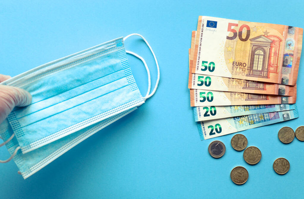 Mascarillas y billetes de euro sobre fondo azul. Compra de mascarillas. En euros. El precio de las mascarillas. - Photo, image