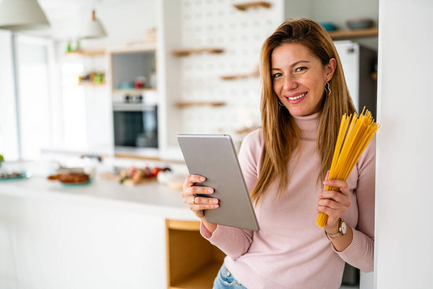 Smiling woman looking at recipe on digital tablet, preparing to cook in kitchen - 写真・画像