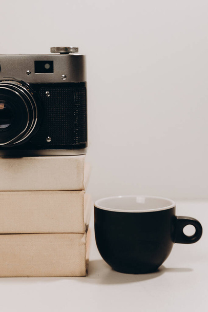 Μαύρο φλιτζάνι καφέ με παλιά vintage κάμερα και λευκά βιβλία σε γκρι απομονωμένο φόντο - Φωτογραφία, εικόνα