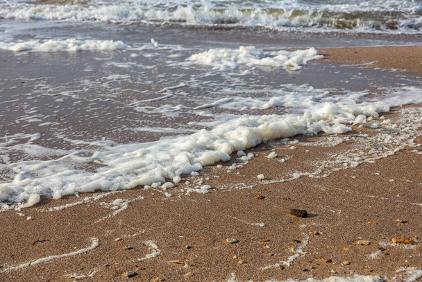 Морська хвиля проходить на пісок пляжу з піною на березі. Морський пейзаж в кольорах заходу сонця. Красивий природний фон для дизайну та оздоблення
 - Фото, зображення