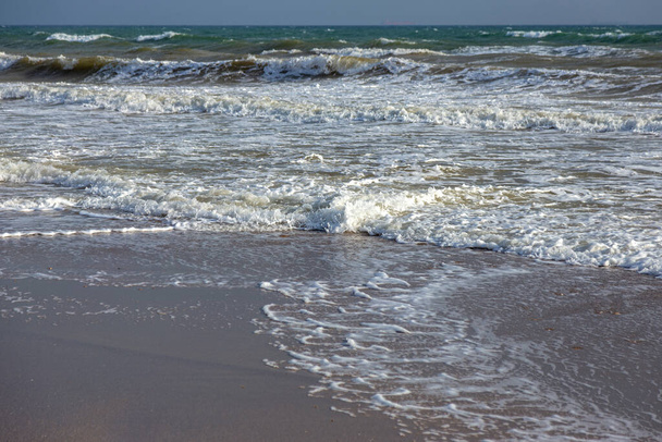 Eine Meereswelle läuft auf den Sand eines Strandes mit Schaum an Land. Seelandschaft in den Farben des Sonnenuntergangs. Schöner natürlicher Hintergrund für Design und Dekoration - Foto, Bild