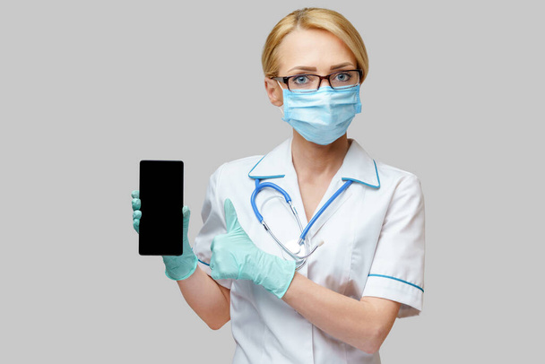 medical doctor nurse woman wearing protective mask and gloves - using mobile phone - Fotó, kép