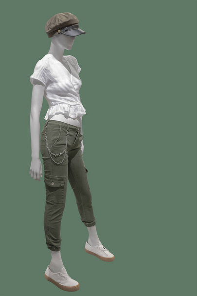 Полноразмерный женский манекен, одетый в модную одежду, выделенный на зеленом фоне. Нет фирменных наименований или объектов авторского права. - Фото, изображение