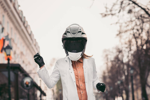 стройная девушка в белом медицинском халате и комбинезоне держит шприц. Женщина в мотоциклетном шлеме в медицинской маске. На её руках латексные перчатки. коронавирус, инфекция, карантин, ковид-19
 - Фото, изображение