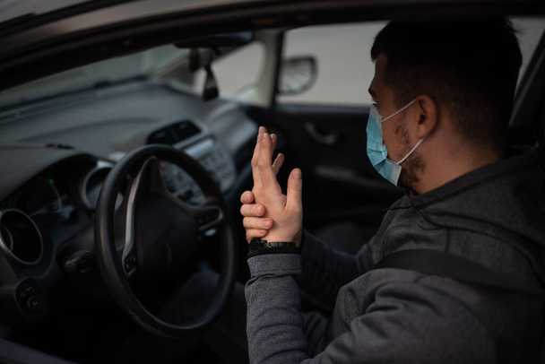 Un hombre se sienta en el coche y se lava las manos con gel antiséptico. concepto de salud en el coche. La máscara es blanca en la cara. coronavirus, enfermedad, infección, cuarentena, covid-19
 - Foto, imagen