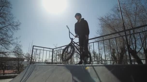 Nuori BMX ratsastaja seisoo rampin päällä ja valmistautuu temppuja äärimmäisessä puistossa
 - Materiaali, video