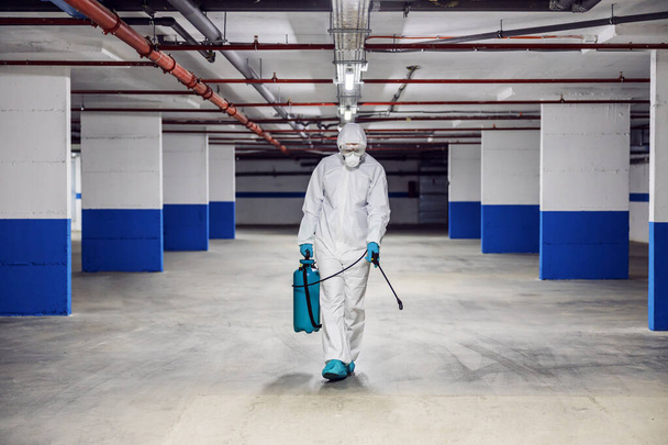 Man in protective suit and mask sterilizing garage from corona virus/ covid 19. - Valokuva, kuva