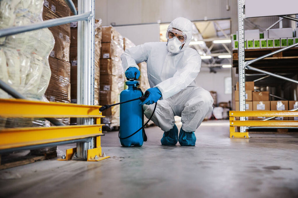 Homme en combinaison de protection et masque désinfectant entrepôt plein de produits alimentaires du virus corona / covid-19. - Photo, image