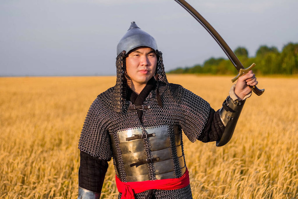 A medieval nomad warrior in oriental armor on the background of a wheat field. Standing in a fencing rack. - Fotografie, Obrázek