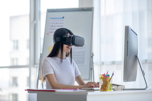 Dark-haired girl working at the computer wearing vr headset - Fotoğraf, Görsel