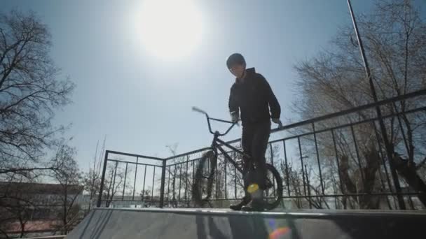 Genç bir BMX sürücüsü rampanın tepesinde duruyor ve ekstrem parktaki ön tekerleği döndürüyor. - Video, Çekim
