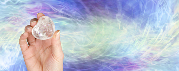 Crystal healer κρατώντας σαφή χαλαζία σφύρα καρδιά πέτρα στολίδι - θηλυκό χέρι που προσφέρει μια μεγάλη καρδιά σχήμα κρύσταλλο σε ένα πράσινο μπλε μωβ φόντο σχηματισμού ενέργειας με αντίγραφο χώρο - Φωτογραφία, εικόνα