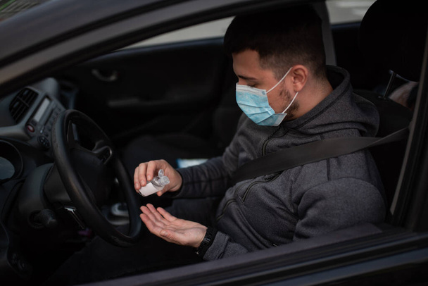 A man use an antiseptic gel into his hands while sitting in a car. A man in a medical mask to protect viruses. masked man in a car. coronavirus, disease, infection, quarantine, covid-19 - Photo, Image