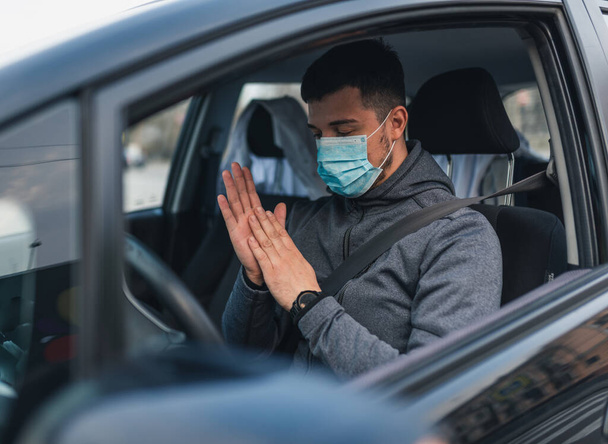 Egy férfi leül, és fertőtlenítő géllel mossa a kezét. egészségügyi koncepció az autóban. A maszk fehér az arcán. coronavirus, betegség, fertőzés, karantén, covid-19 - Fotó, kép