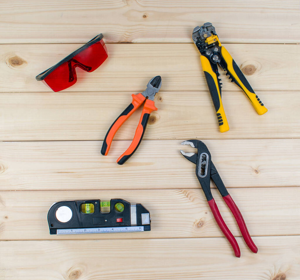 Set of tools for repai and carpentry. Red protective glasses, flat-nose pliers, adjustable spanner, key, roulette and level. Top view of carpenter's tools on wooden background. Construction industry, diy.  - Photo, Image