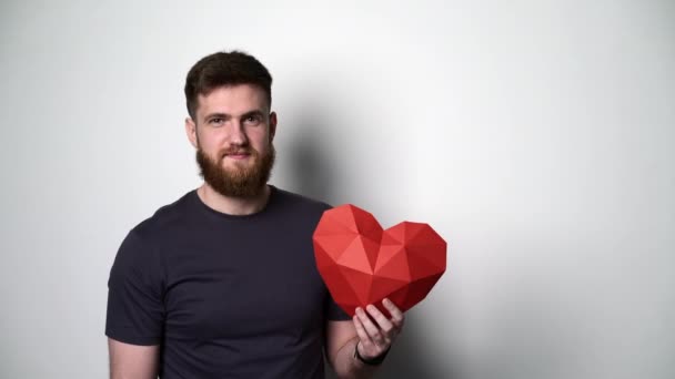Μισού μήκους πορτρέτο του νεαρού γενειοφόρου hipster άνθρωπος κρατώντας κόκκινο σχήμα καρδιάς - Πλάνα, βίντεο