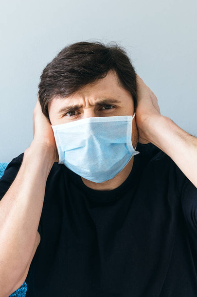 Male in blue medical face mask holding his head with his hands. Man in shock, stay at home during quarantine - Фото, изображение