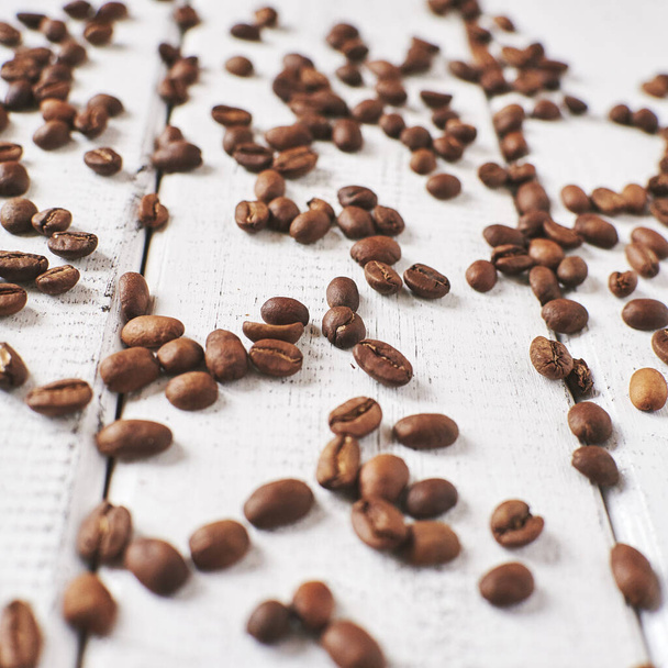 Roasted coffee beans are scattered on the white wooden surface - Photo, Image