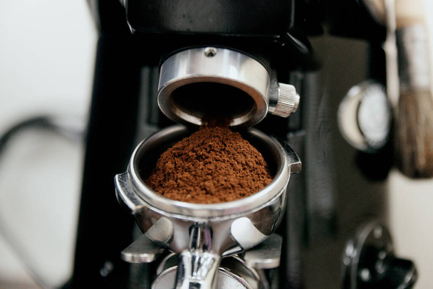 Процесс автоматического измельчения кофе в кофемолке крупным планом. Горстка молотого кофе в держателе
 - Фото, изображение