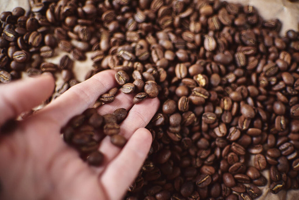 Горстка коричневых кофейных зерен в ладони рядом с чашкой эспрессо
 - Фото, изображение