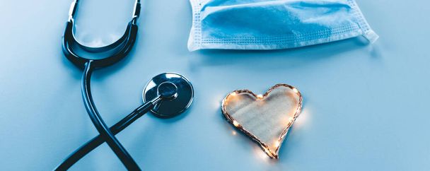 Kartondoboz szív koszorúval, orvosi maszkkal és sztetoszkóppal kék alapon - Fotó, kép