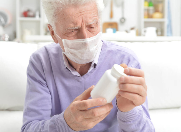 Portrait of sad sick senior man with facial mask  holding pills - Фото, зображення