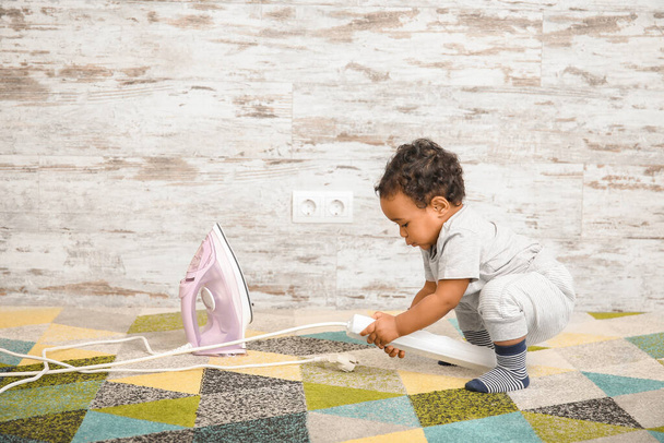 Um bebé afro-americano a brincar com ferro em casa. Criança em perigo
 - Foto, Imagem