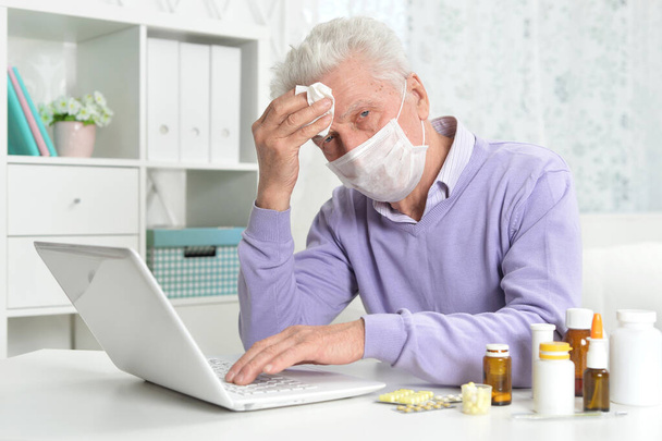  sick senior man with facial mask using laptop - Fotó, kép