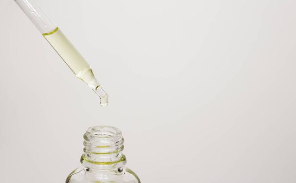 El aceite cosmético gotea de una pipeta en un frasco de vidrio. Aceite para el cabello y la piel. Tratamientos de spa, cuidado de la piel y el cabello
. - Foto, Imagen