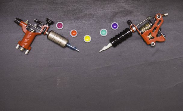 Περιστροφικά και επαγωγικά μηχανήματα τατουάζ και χρωματιστά χρώματα σε πλαστικά βάζα σε μαύρο φόντο. Ελεύθερος χώρος για κείμενο. Η θέα από την κορυφή. - Φωτογραφία, εικόνα