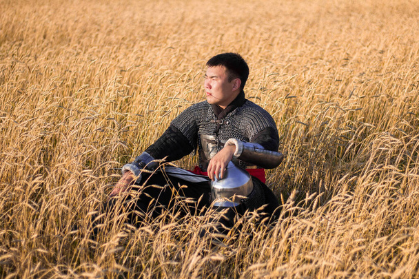 Asian warrior in oriental armor and with a saber in his hands sitting in a wheat field. - Fotó, kép