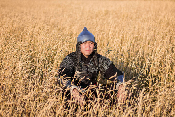 Asian warrior in oriental armor and with a saber in his hands sitting in a wheat field. - Фото, зображення