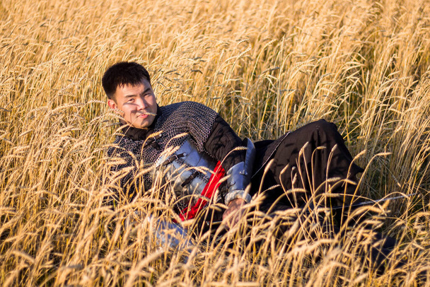 Азіатський воїн у східному обладунку і з шаблею в руках сидячи на полі пшениці.. - Фото, зображення