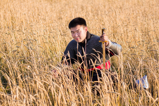 Asian warrior in oriental armor and with a saber in his hands sitting in a wheat field. - Fotografie, Obrázek