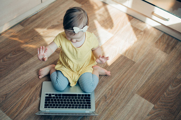 Lovely toddler sitting on her knees in front of a laptop and putting both hands up - Photo, Image