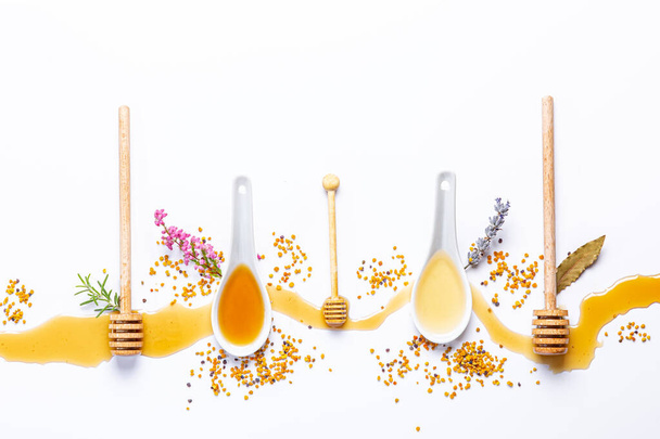 white spoons and honey sticks, with spilled honey, bee pollen and flowers isolated on white background - Photo, Image