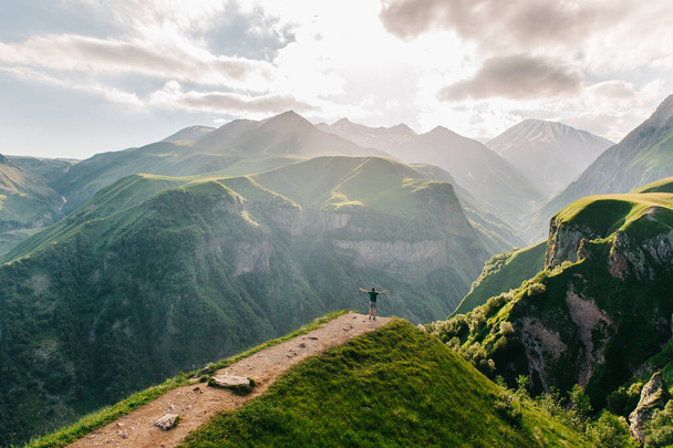 A traveler on the edge of a cliff with a spectacular view behind him. Amazing view of the Devil's Valley in the mountains of the Caucasus. Georgian military road in Georgia, beautiful mountains - 写真・画像