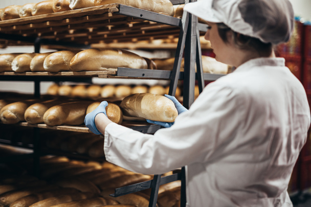 Jonge werkneemster in de bakkerij. Ze legt brood op de plank.. - Foto, afbeelding