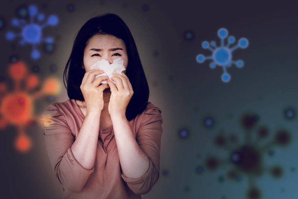 sick Asian woman suffering from covid 19 virus hand holding paper tissue and sneezing or coughing with viruses spreading in background - Photo, Image