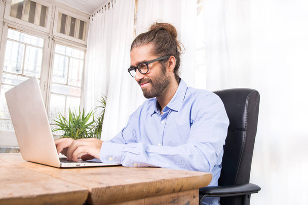 hombre de pelo largo trabajando con su portátil en una oficina
 - Foto, imagen
