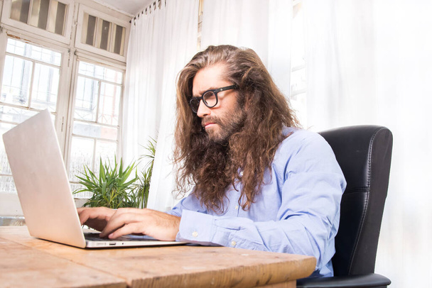 man met lang haar werken met zijn laptop in een kantoor - Foto, afbeelding