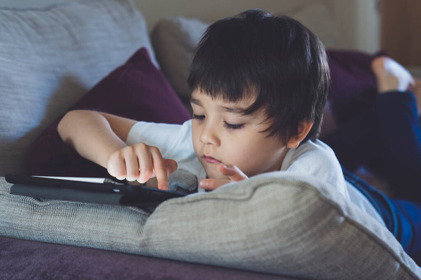 School kid using tablet for homework, Child lying down on sofa tuching on sceeen, Bored Boy stay at home during covid lock down,Social Distancing, learning online , Distnace Educationeducation concept - Photo, Image