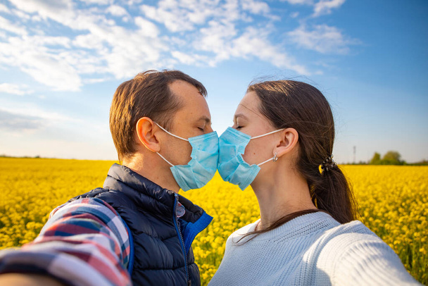 Pareja enamorada, hombre y mujer besándose en máscara médica protectora en la cara en el campo
 - Foto, imagen