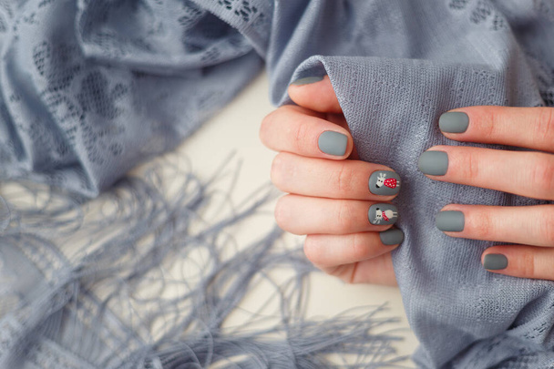 Vrouwelijke handen met vrolijk kerstrendier manicure op vingernagels met grijze sjaal. Nieuwjaar, wintervakantie, spijker- en handverzorging, beauty en fashion concept. - Foto, afbeelding