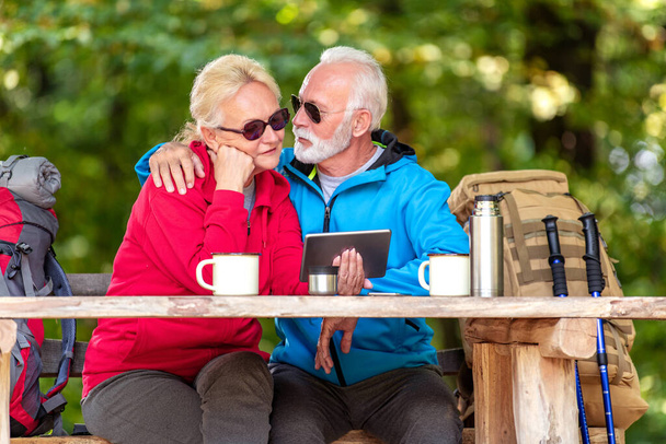 Senior couple using tablet while hiking in the forest. - Foto, Imagen