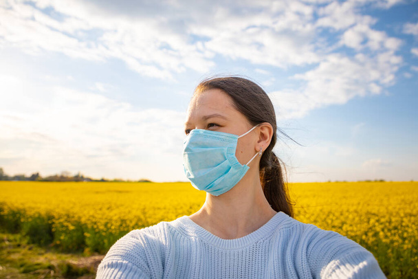 Nő védő orvosi maszk az arcon vidéken repcemag mező és kék ég a háttérben - Fotó, kép