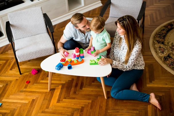 Χαριτωμένο μικρό αγόρι παίζει με τα παιχνίδια στο σαλόνι με τον πατέρα και τη μητέρα - Φωτογραφία, εικόνα